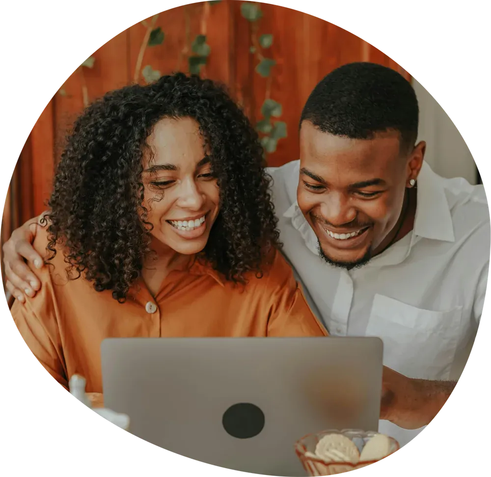 A couple smiling together at a laptop, looking at therapy options.
